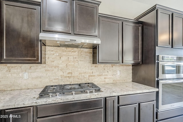 kitchen with under cabinet range hood, appliances with stainless steel finishes, backsplash, and dark brown cabinetry
