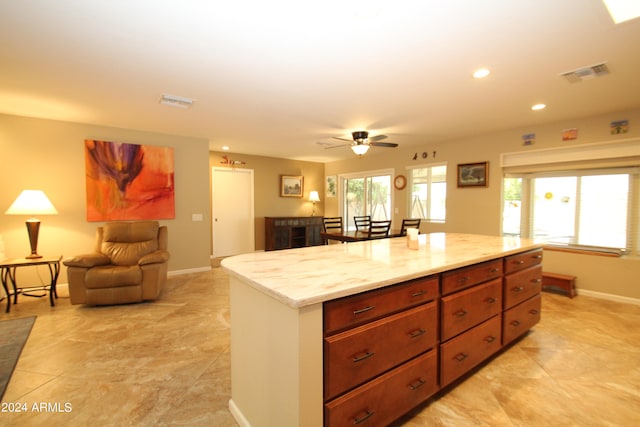 kitchen with light stone countertops, a center island, and ceiling fan