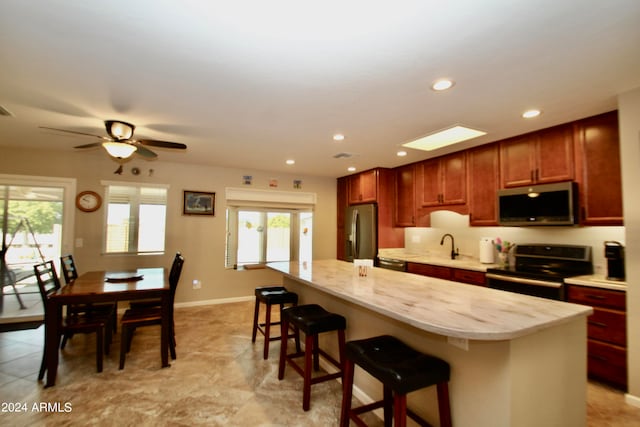 kitchen featuring a kitchen island, stainless steel appliances, a breakfast bar, light stone counters, and ceiling fan