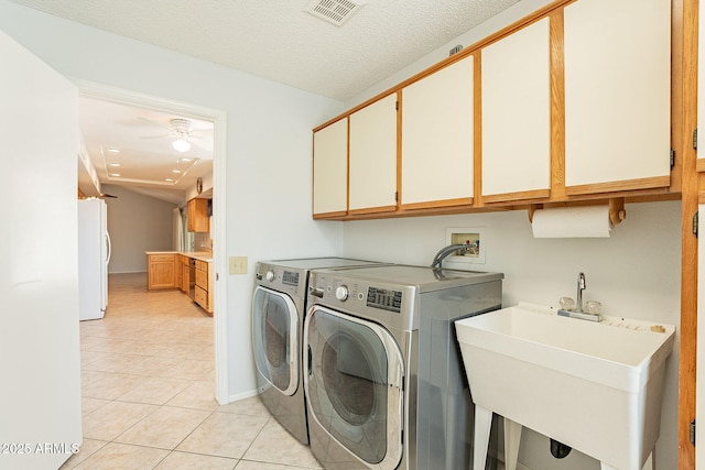 washroom with light tile patterned flooring, sink, cabinets, separate washer and dryer, and a textured ceiling