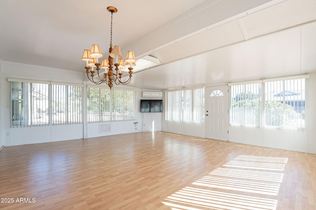 unfurnished living room with a wealth of natural light, a wall unit AC, hardwood / wood-style floors, and a chandelier