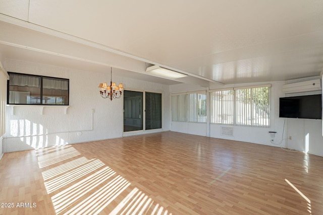 unfurnished living room featuring wood-type flooring, a wall mounted air conditioner, and a notable chandelier