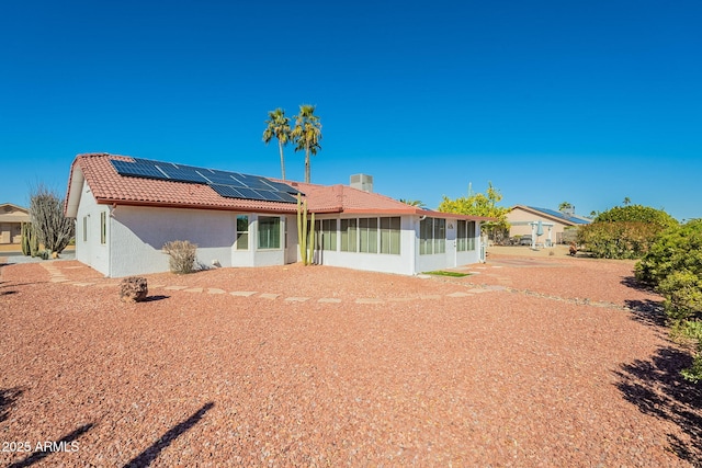 back of property with a sunroom and solar panels