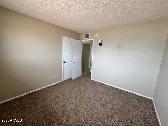 unfurnished bedroom featuring a textured ceiling and dark colored carpet