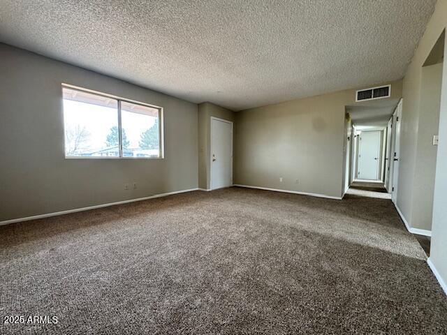 spare room featuring a textured ceiling and dark colored carpet