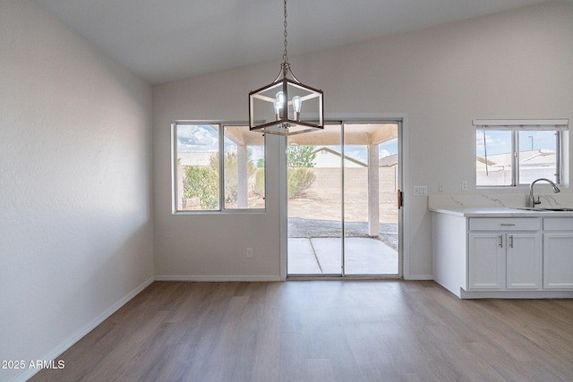 unfurnished dining area featuring sink, lofted ceiling, a chandelier, and light wood-type flooring