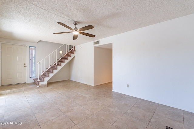 tiled spare room featuring visible vents, ceiling fan, a textured ceiling, and stairs