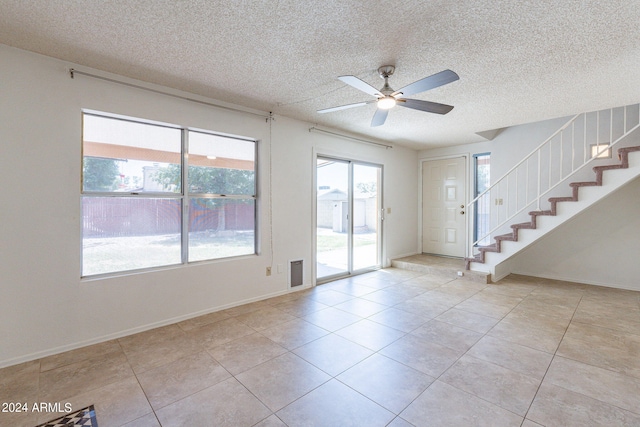 entryway with a textured ceiling, ceiling fan, light tile patterned floors, baseboards, and stairway