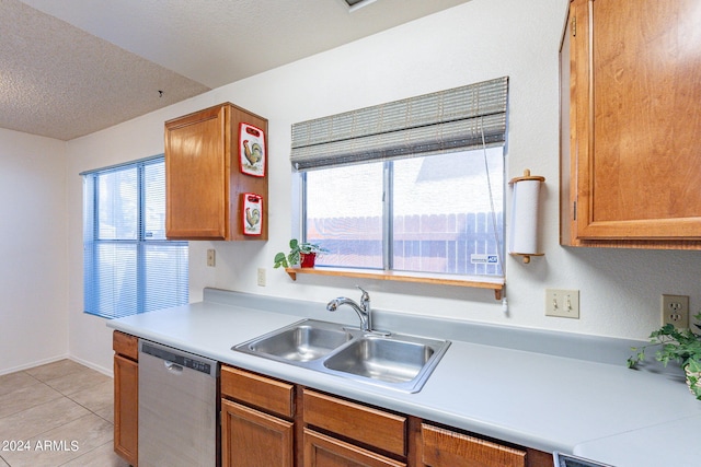 kitchen with light tile patterned floors, a sink, light countertops, stainless steel dishwasher, and brown cabinetry