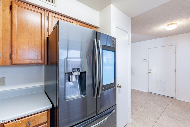 kitchen featuring stainless steel refrigerator with ice dispenser, light tile patterned floors, light countertops, brown cabinetry, and a textured ceiling