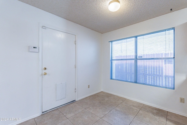 spare room featuring a textured ceiling, light tile patterned flooring, and baseboards