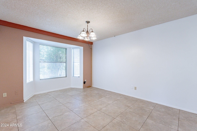 empty room with a chandelier, a textured ceiling, baseboards, and light tile patterned floors