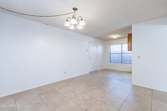 empty room with a chandelier, light tile patterned flooring, a textured ceiling, and baseboards