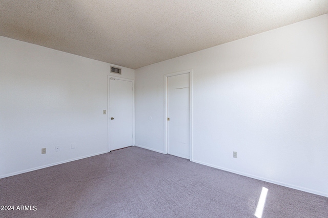 carpeted spare room with baseboards, visible vents, and a textured ceiling