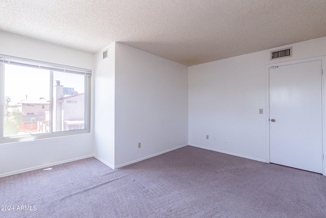 carpeted spare room with visible vents, a textured ceiling, and baseboards