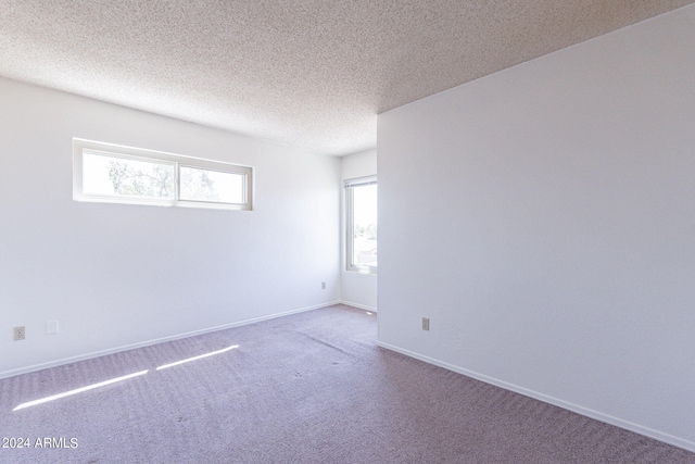 carpeted empty room featuring a textured ceiling and baseboards