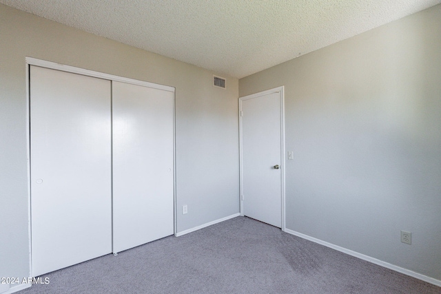 unfurnished bedroom with baseboards, visible vents, a textured ceiling, carpet floors, and a closet