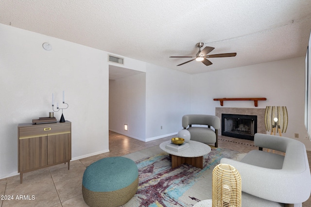 living room featuring light tile patterned floors, visible vents, a tiled fireplace, a ceiling fan, and a textured ceiling