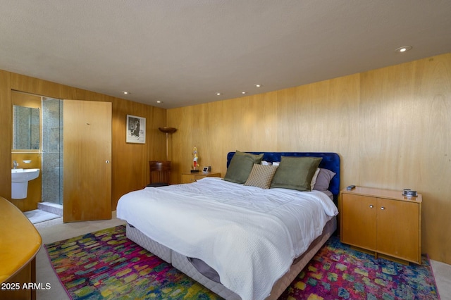 bedroom featuring ensuite bath, light colored carpet, and wooden walls