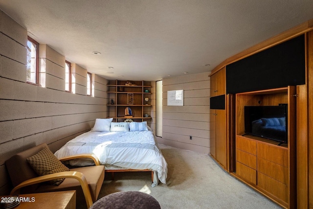 bedroom with wood walls, a textured ceiling, and light carpet