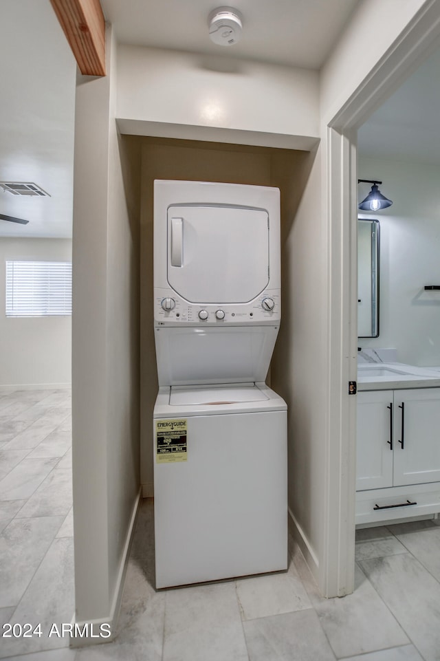 laundry room featuring stacked washing maching and dryer and light tile floors