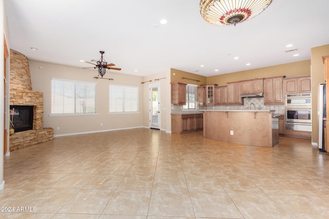 kitchen featuring ceiling fan, light tile patterned floors, backsplash, a fireplace, and a kitchen island