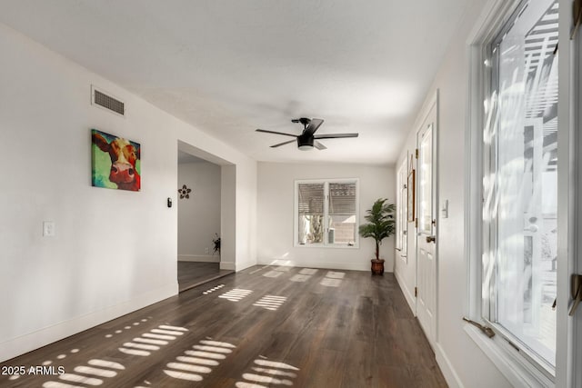 empty room featuring a ceiling fan, baseboards, visible vents, and dark wood-style flooring