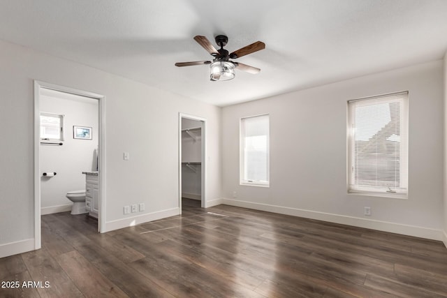 unfurnished bedroom featuring a closet, a spacious closet, baseboards, and dark wood-type flooring