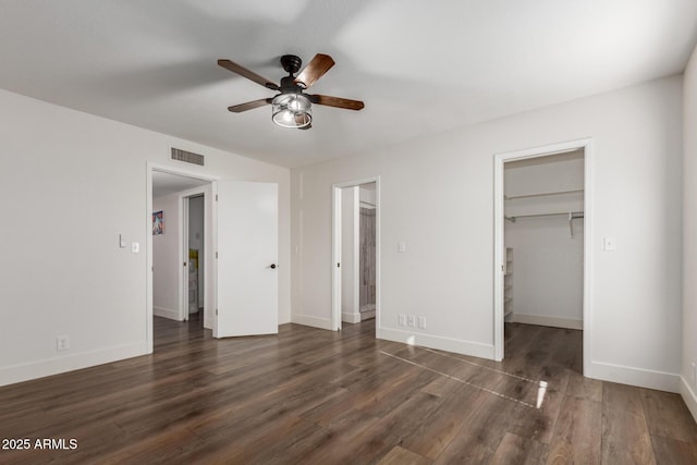 unfurnished bedroom with dark wood-style floors, visible vents, a spacious closet, a ceiling fan, and baseboards