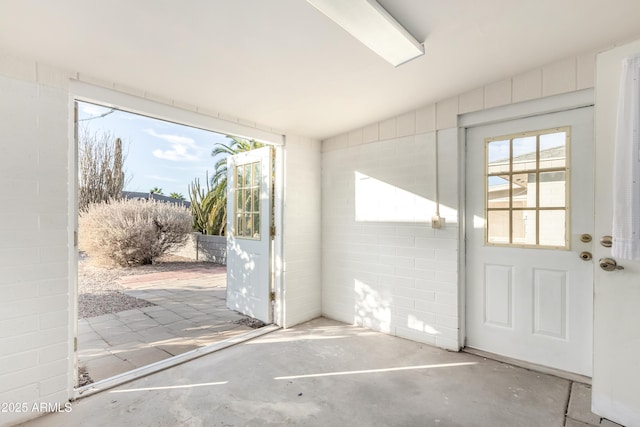 doorway to outside with a healthy amount of sunlight, unfinished concrete floors, and concrete block wall