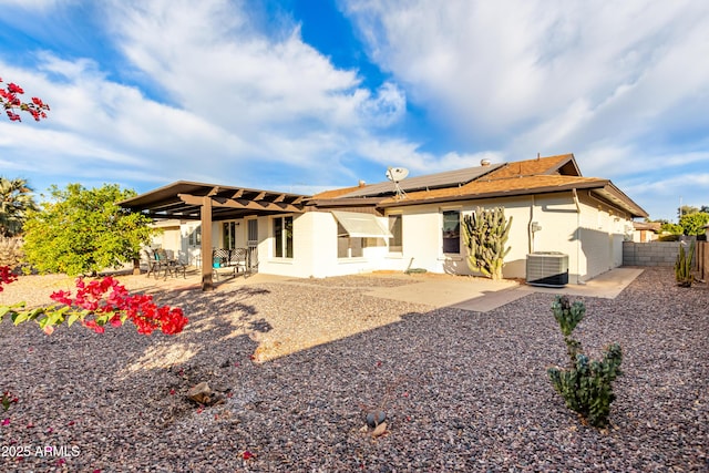 rear view of house featuring a patio, a fenced backyard, roof mounted solar panels, central AC, and stucco siding