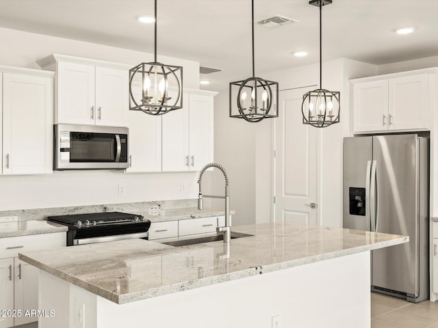 kitchen with appliances with stainless steel finishes, a center island with sink, white cabinets, and decorative light fixtures