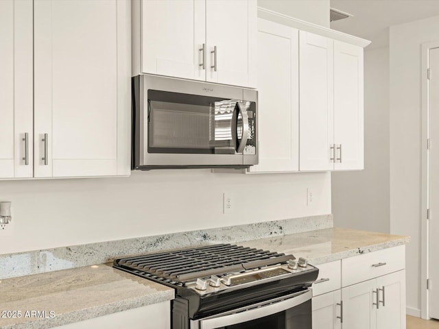 kitchen with appliances with stainless steel finishes, white cabinets, and light stone counters