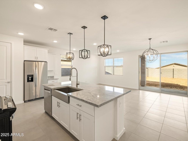 kitchen featuring white cabinetry, stainless steel appliances, decorative light fixtures, and an island with sink