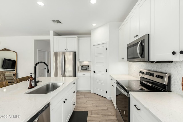 kitchen with stainless steel appliances, visible vents, decorative backsplash, a sink, and light wood-type flooring