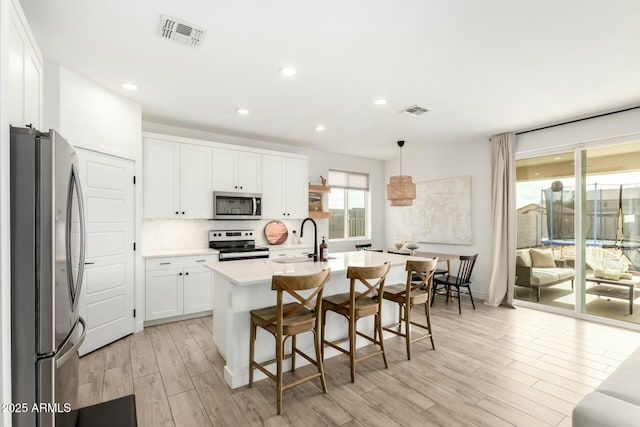 kitchen with appliances with stainless steel finishes, visible vents, a sink, and tasteful backsplash