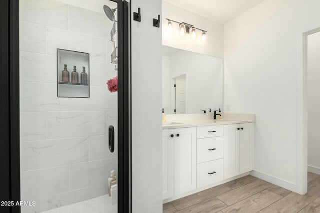 bathroom featuring wood finished floors, a sink, baseboards, double vanity, and a stall shower