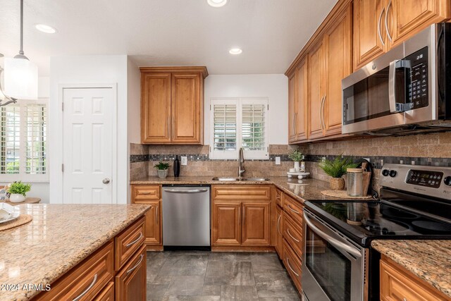 kitchen with decorative light fixtures, stainless steel appliances, sink, and light stone counters