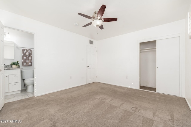 unfurnished bedroom with a closet, ensuite bath, light colored carpet, and ceiling fan