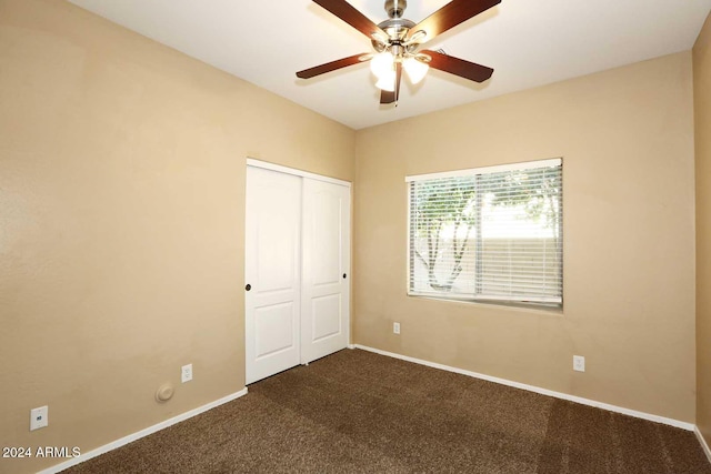 unfurnished bedroom with ceiling fan, dark carpet, and a closet