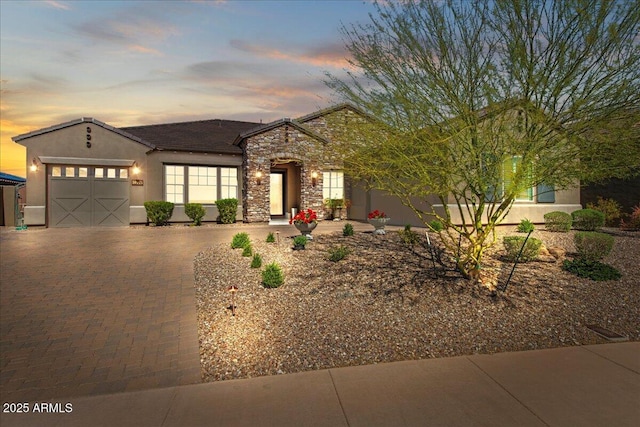 view of front of house featuring a tile roof, stone siding, stucco siding, decorative driveway, and a garage