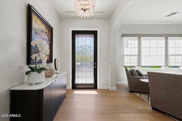 foyer entrance with a raised ceiling, a chandelier, light wood-style flooring, baseboards, and visible vents