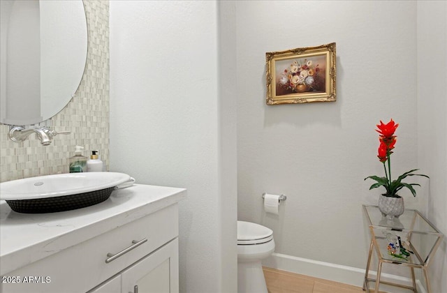 half bathroom featuring baseboards, toilet, vanity, and tasteful backsplash