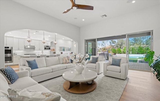 living area featuring high vaulted ceiling, light wood-style flooring, ceiling fan with notable chandelier, arched walkways, and recessed lighting