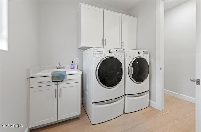 laundry room featuring baseboards, a sink, light wood finished floors, cabinet space, and washer and dryer
