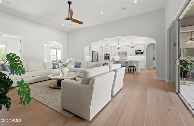 living area featuring light wood-style flooring, plenty of natural light, arched walkways, and ceiling fan with notable chandelier