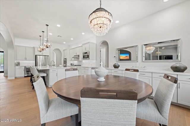 dining room with an inviting chandelier, arched walkways, light wood finished floors, and beverage cooler