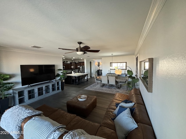 living area featuring a ceiling fan, visible vents, crown molding, and a textured ceiling