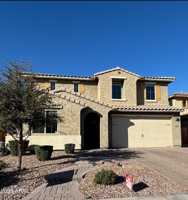 mediterranean / spanish-style house featuring an attached garage, a tile roof, decorative driveway, and stucco siding