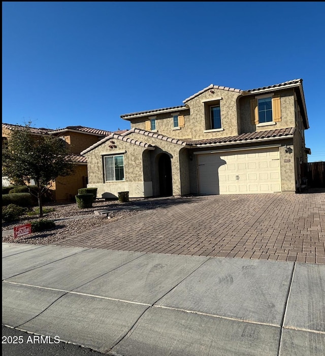 mediterranean / spanish-style house featuring stone siding, a tile roof, an attached garage, decorative driveway, and stucco siding